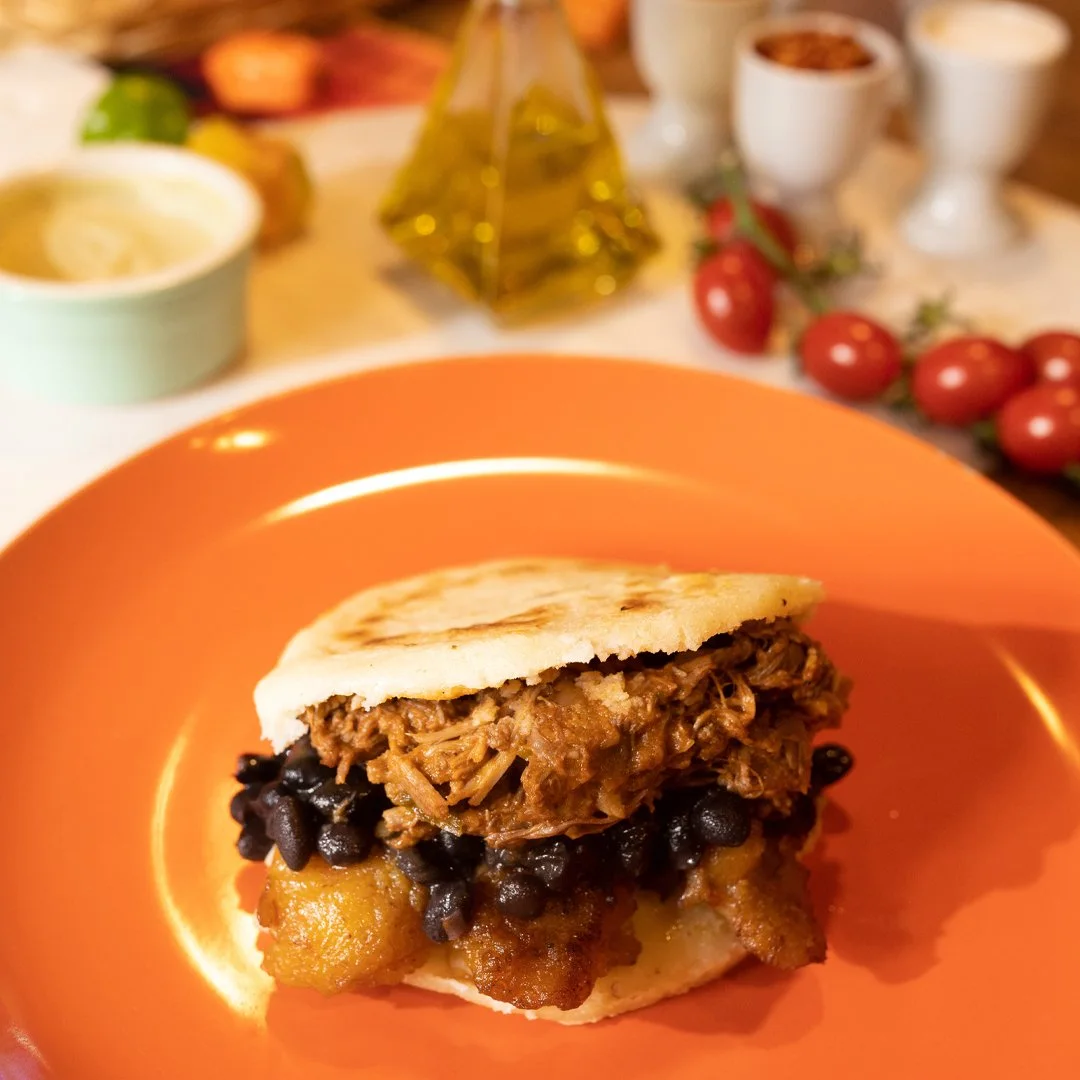 An arepa filled with shredded beef and black beans on an orange plate.