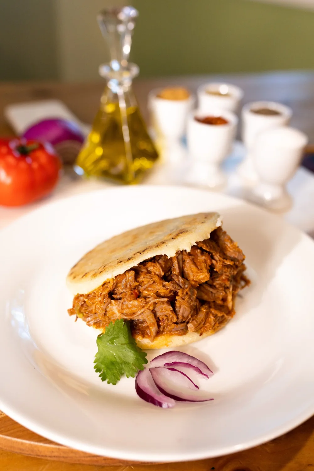 A griddled arepa split open and filled with shredded beef, garnished with cilantro and red onion.