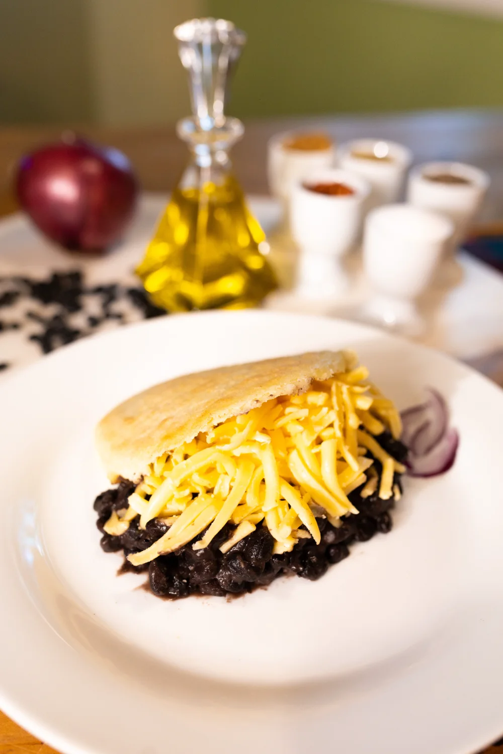 An arepa filled with shredded cheese on a plate of black beans.