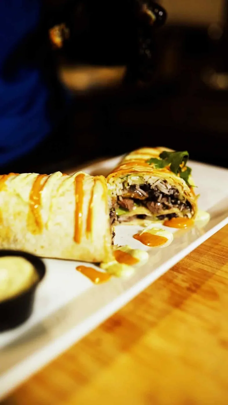A wrap cut open to show steak, rice, beans and lettuce, drizzled with house sauce.