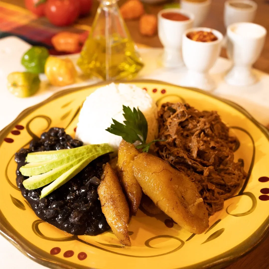 Black beans, white rice, shredded beef and fried sweet plantains on a yellow patterned plate.