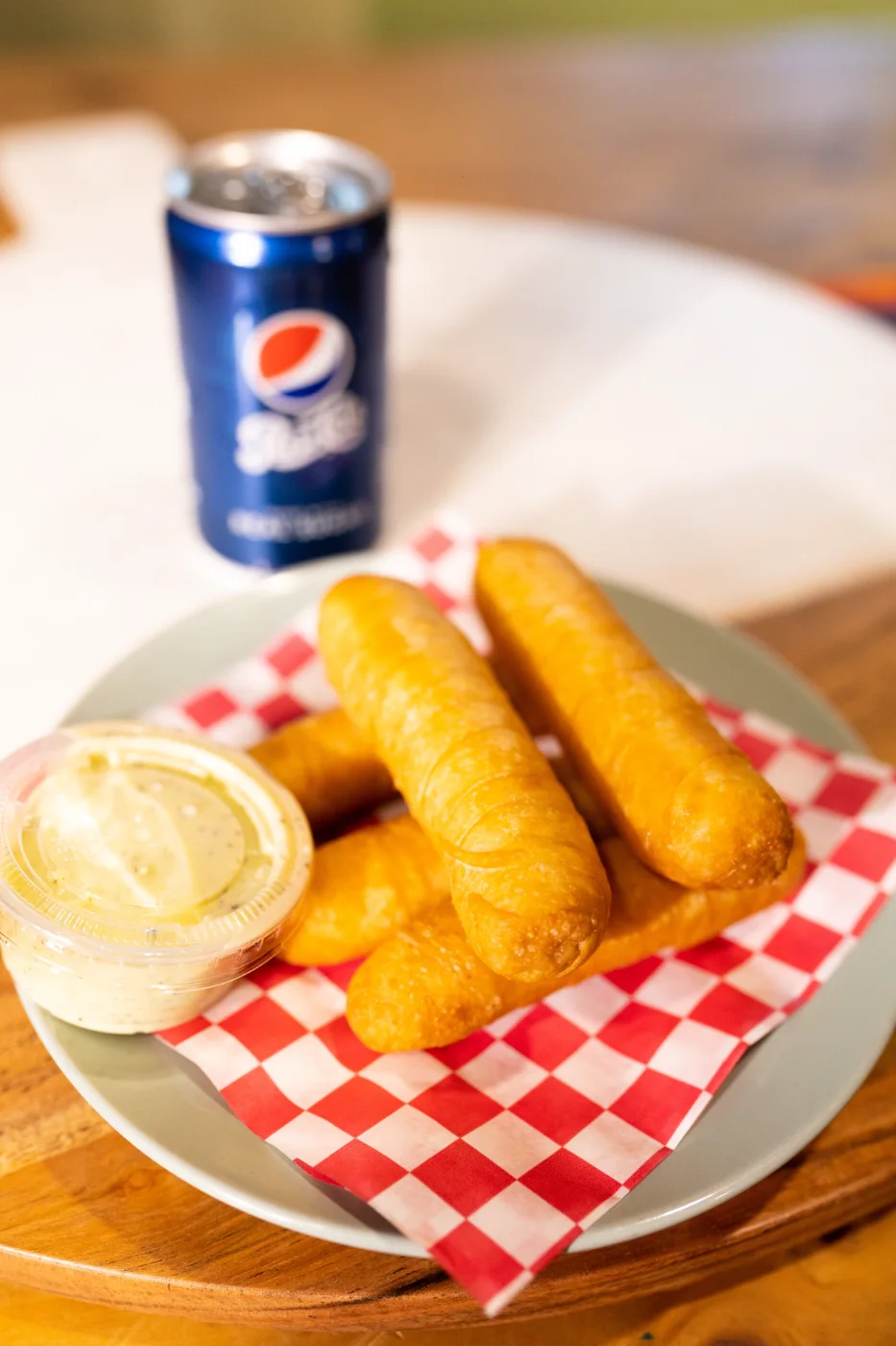 Four tequeños on checkered paper with a cup of dipping sauce.